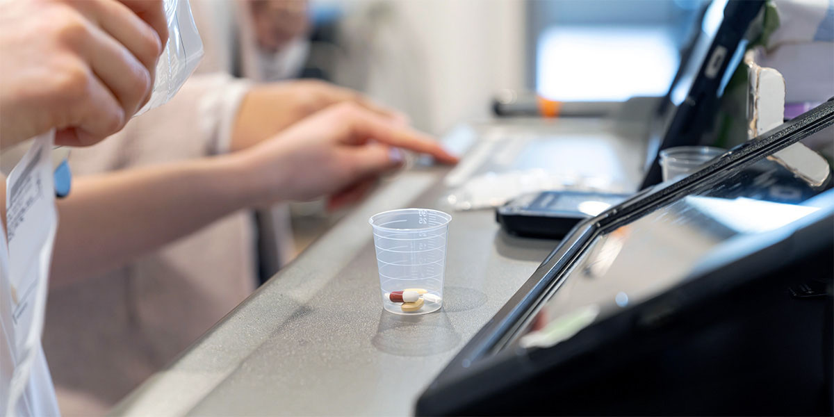 shot of people working in facility with prescription drugs in cup on counter